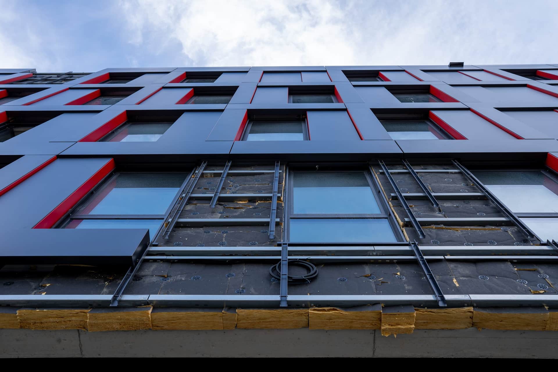 Metallfassade aus anthrazitfarbenen Kassetten mit roten Akzenten, Frontansicht