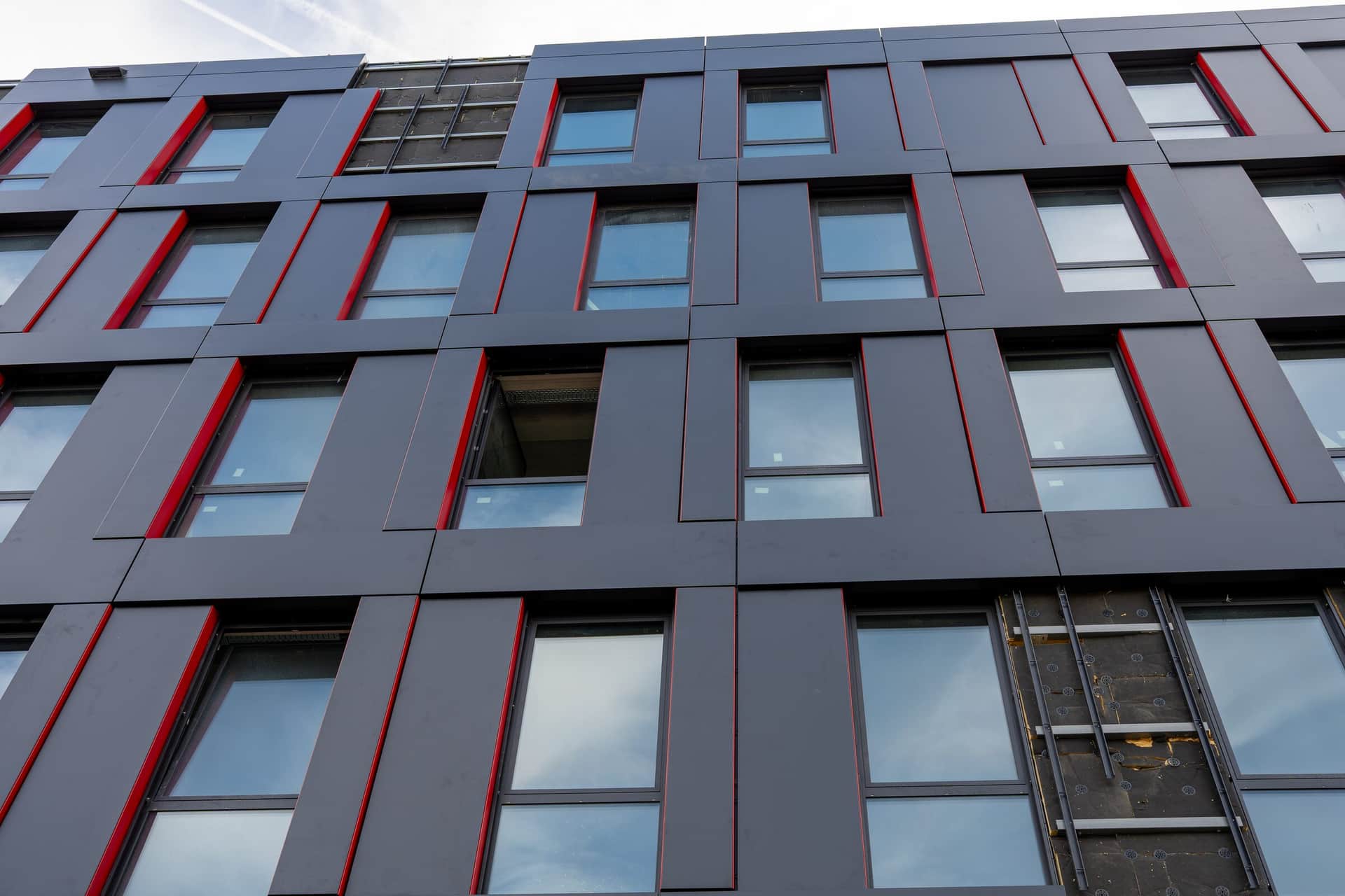 Anthrazitfarbene Metallfassade mit roten Fensterlaibungen in der Untersicht