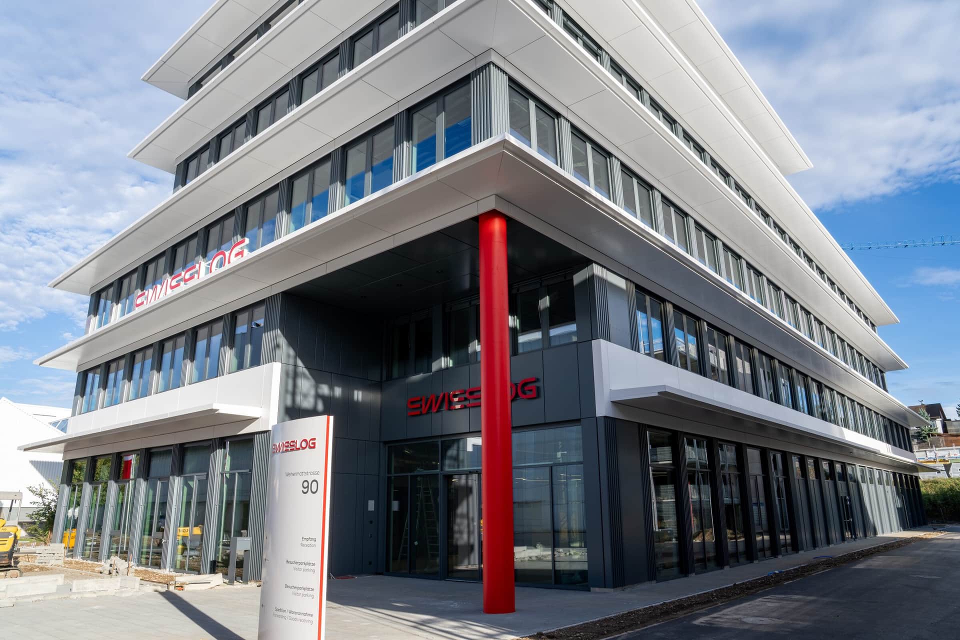 Gebäudeecke mit Metallfassade, roter Stütze und Eingangsbereich