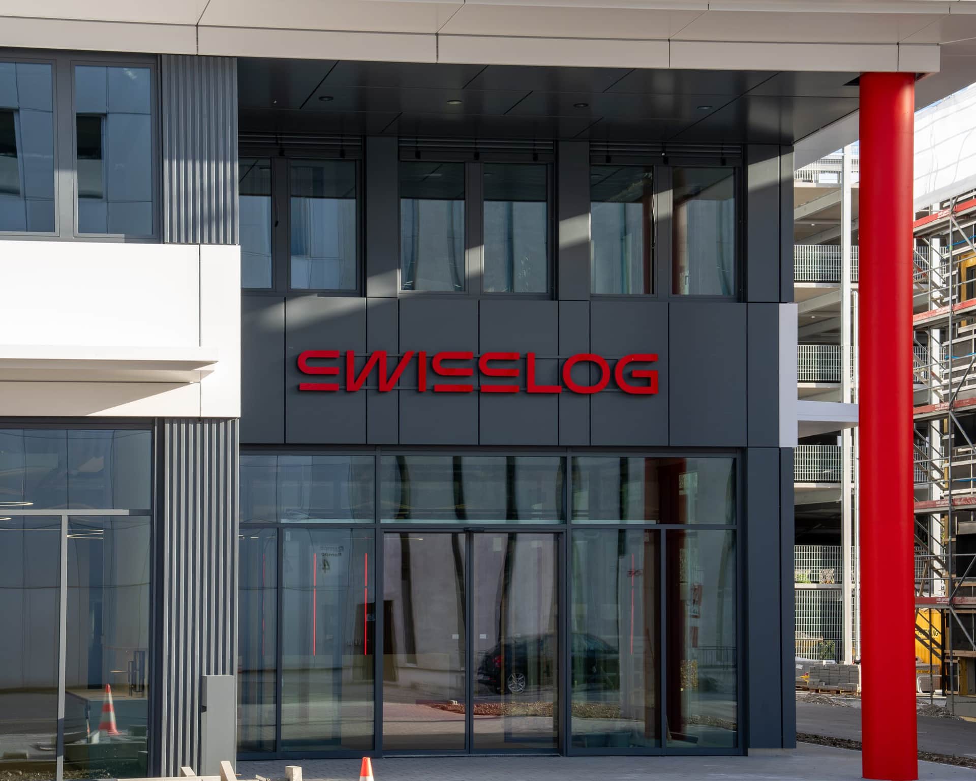 Haupteingang mit anthrazitfarbener Metallfassade und roter Stütze