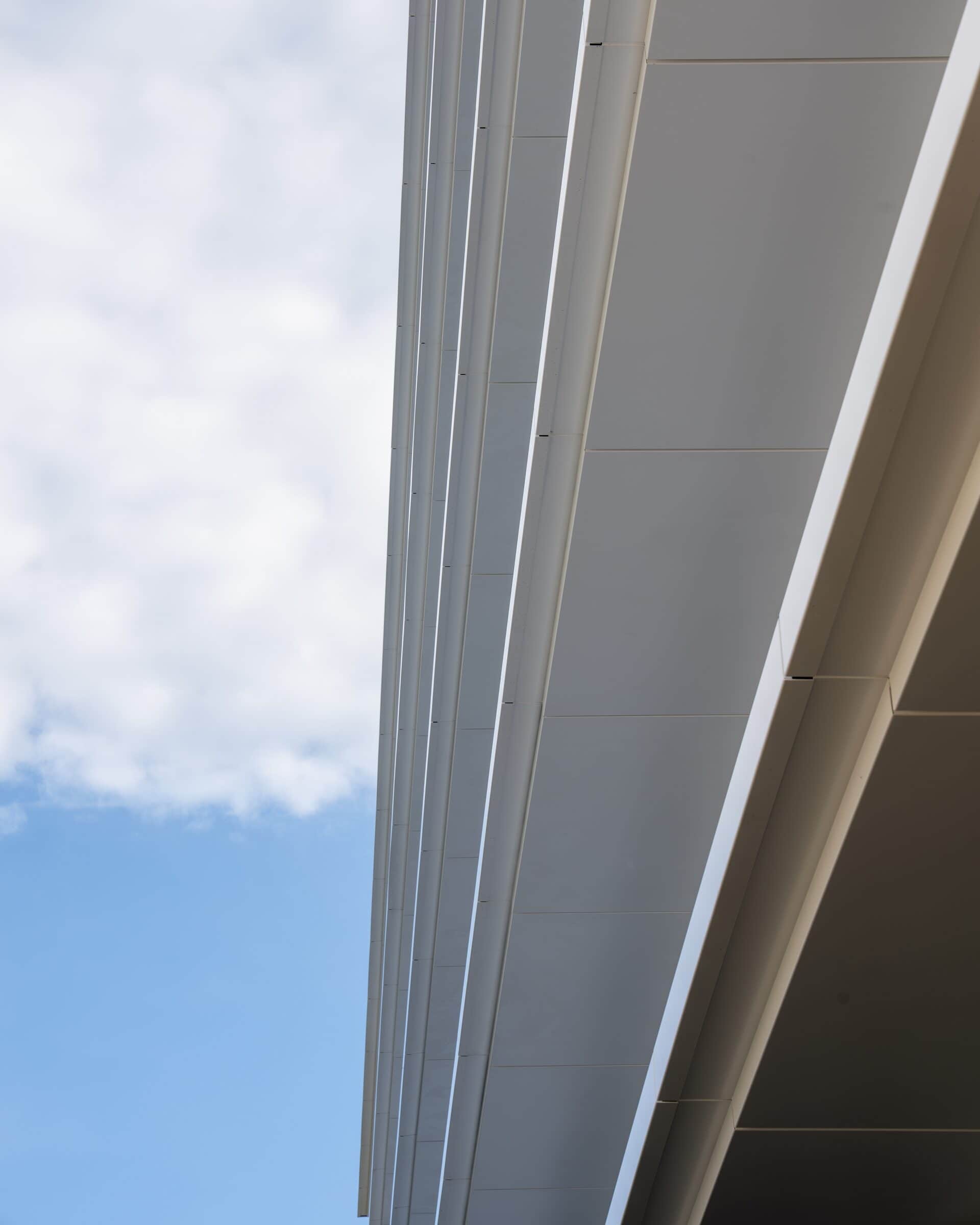 Kantendetail der weissen Blechverkleidung einer Metallfassade vor blauem Himmel