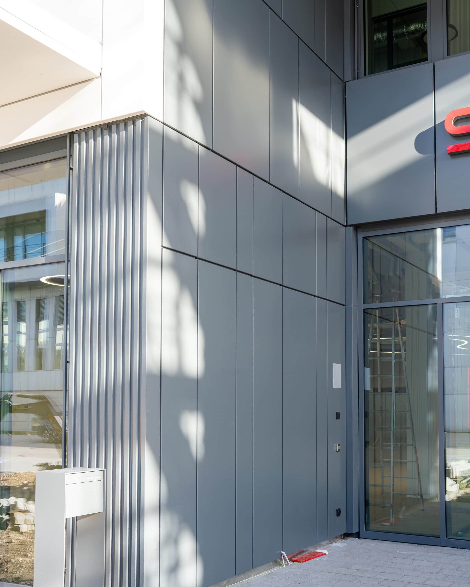 Graue Metallfassade aus Profilblech und Kassetten im Eingangsbereich