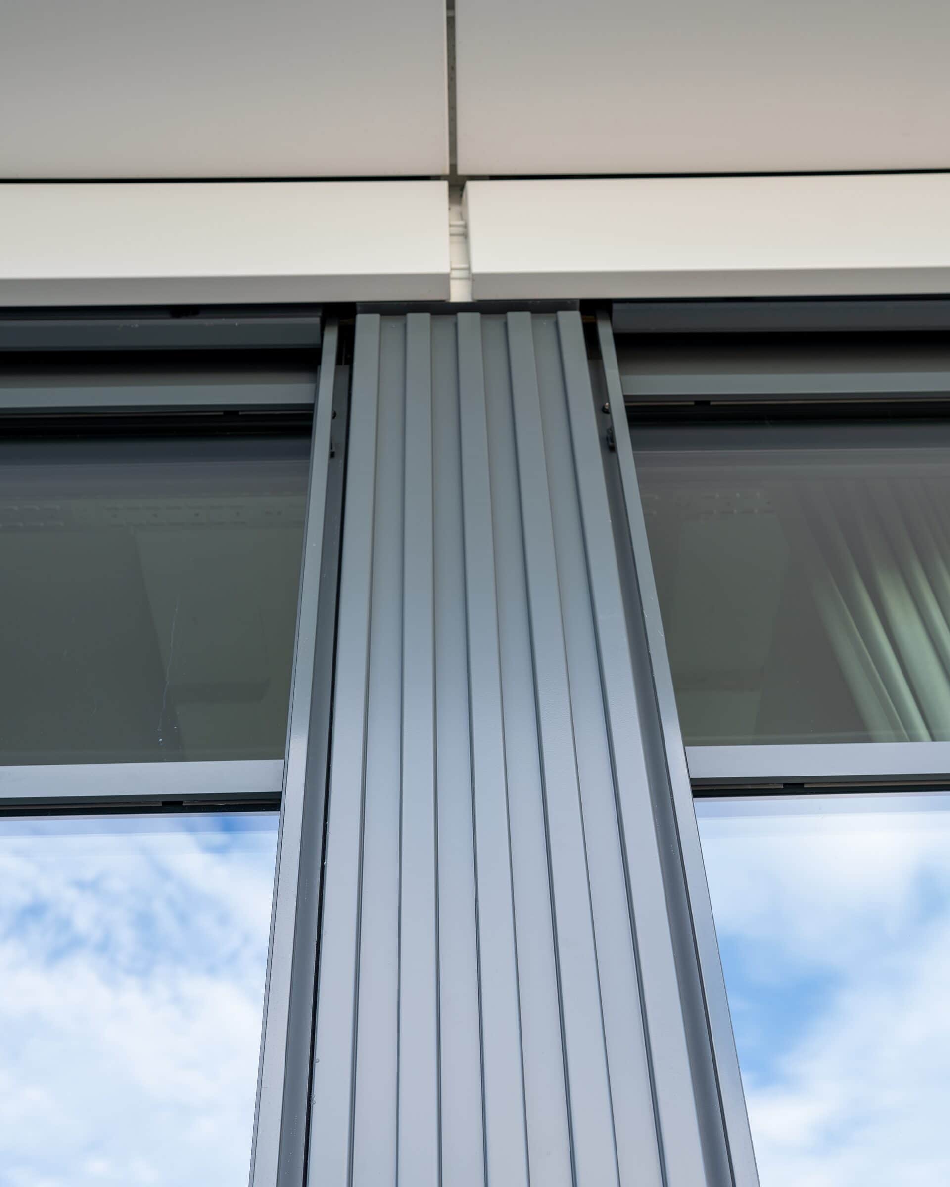 Stützenverkleidung aus grauem Profilblech an einer Metallfassade