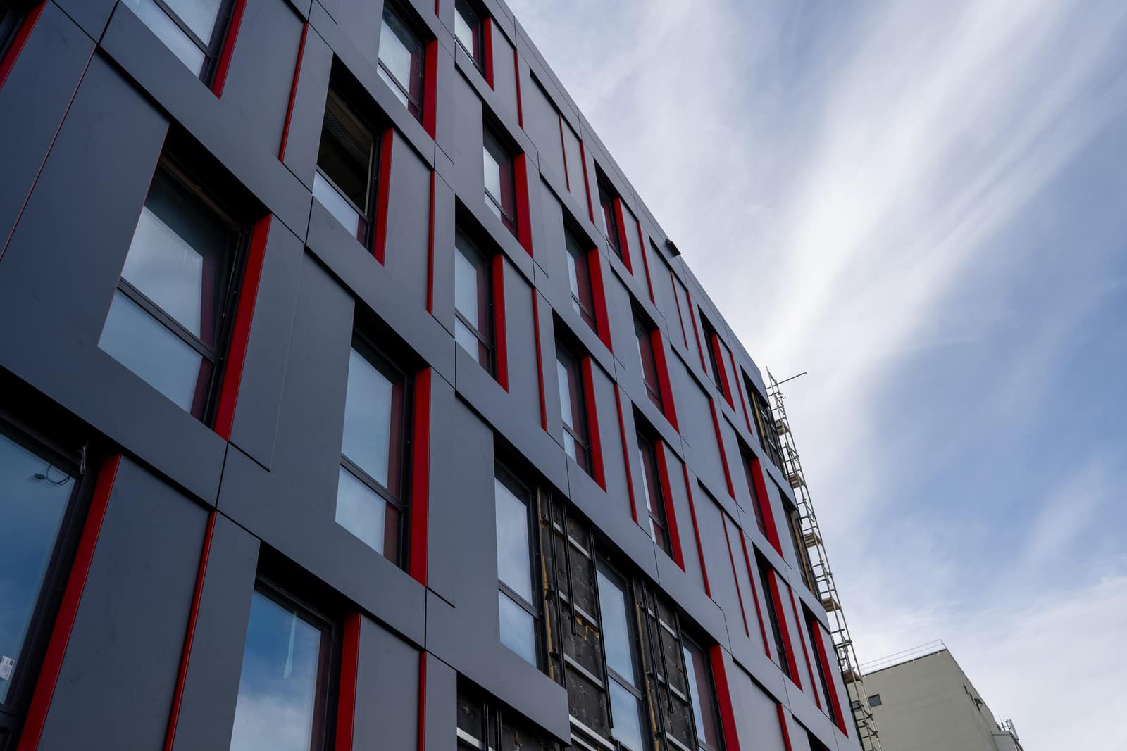 Anthrazitfarbene Metallkassettenfassade mit roten Fensterlaibungen